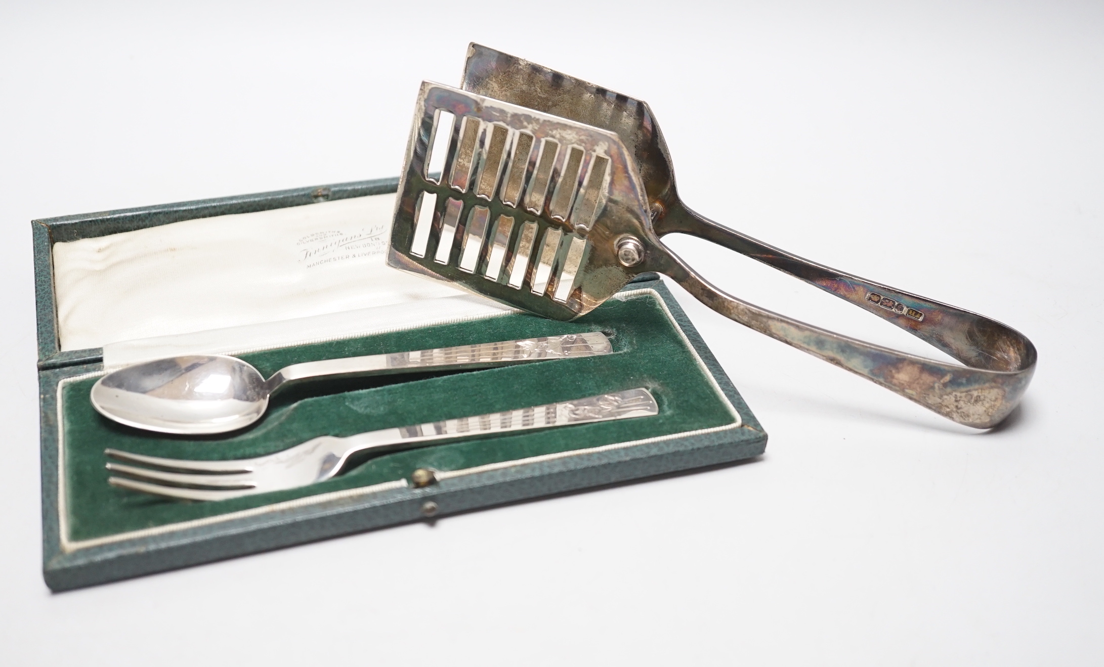 A cased George VI silver christening spoon and fork, by Robert Edgar Stone, London, 1938 and a pair of George V silver asparagus servers.